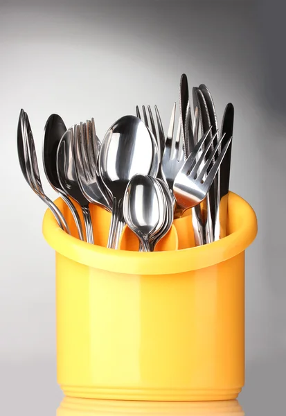 Sztućce kuchenne, noże, widelce i łyżki na żółto stanie na szary troska — Zdjęcie stockowe