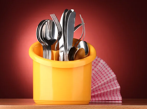 Talheres de cozinha, facas, garfos e colheres em amarelo stand no fundo vermelho — Fotografia de Stock