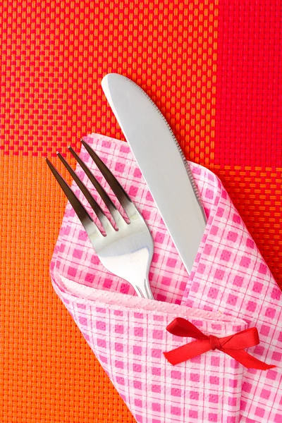 Forchetta e coltello in un panno a quadri con fiocco su una tovaglia rossa — Foto Stock