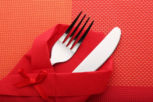 Garfo e faca em um pano vermelho com um arco em uma toalha de mesa vermelha — Fotografia de Stock