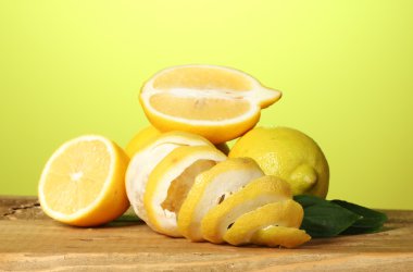 Ripe lemons with leaves on wooden table on green background clipart