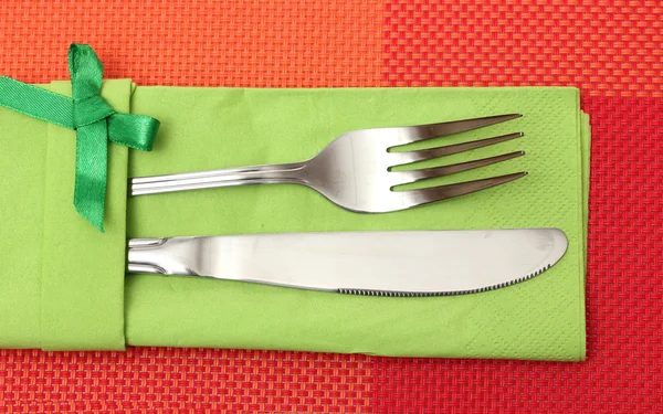Fiyonk kırmızı masa örtüsü üzerinde yeşil bir bezle bıçak ve çatal — Stok fotoğraf