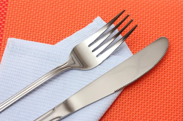 Fork and knife in a blue cloth on a red tablecloth — Stock Photo, Image
