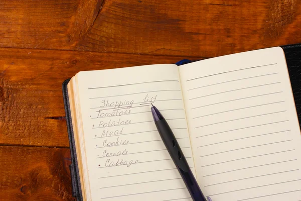 Shoping lista och penna på träbord — Stockfoto