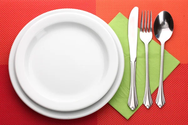 White empty plate with fork, spoon and knife on a red tablecloth — Stock Photo, Image