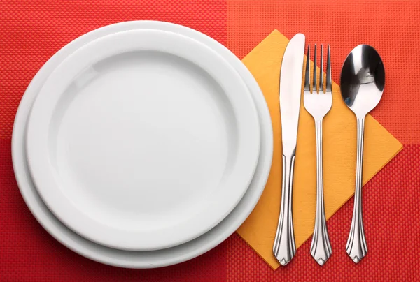 White empty plate with fork, spoon and knife on a red tablecloth — Stock Photo, Image