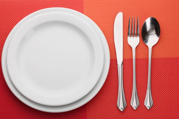 Λευκό άδειο πιάτο με πιρούνι, κουτάλι και μαχαίρι για ένα κόκκινο τραπεζομάντιλο — Φωτογραφία Αρχείου