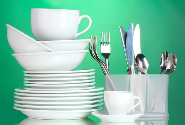 Čisté talíře, šálky a příbory na zeleném pozadí — Stock fotografie