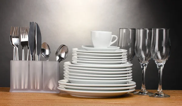 Assiettes, verres, gobelets et couverts propres sur table en bois sur fond gris — Photo