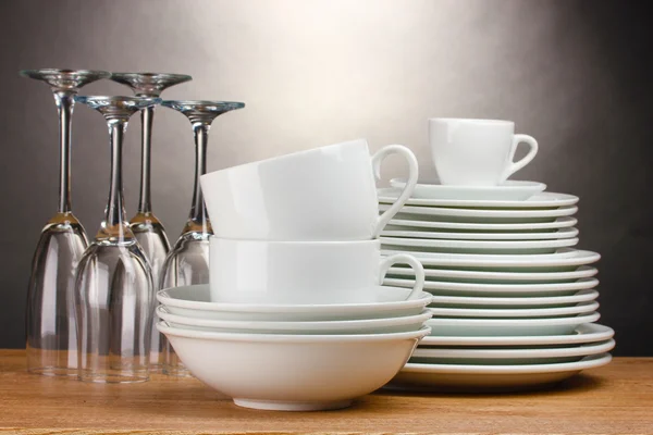 Чистые тарелки, стаканы и чашки на деревянном столе на сером фоне — стоковое фото