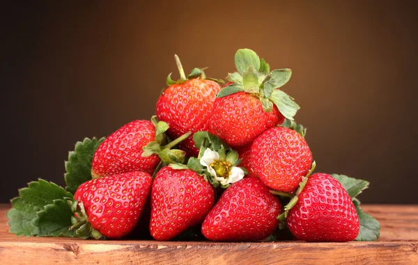 Erdbeeren mit Blättern auf Holztisch auf braunem Hintergrund — Stockfoto