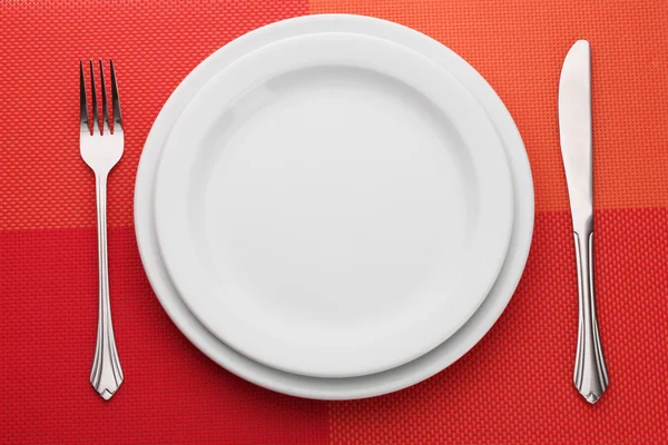 Біла порожня тарілка з виделкою і ножем на червоній скатертині — стокове фото