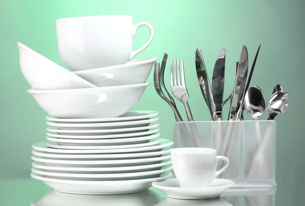Чистые тарелки, чашки и столовые приборы на зеленом фоне — стоковое фото
