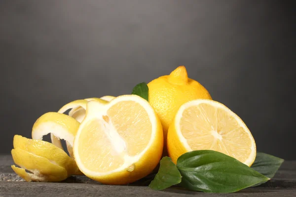 Спелые лимоны с листьями на деревянном столе на сером фоне — стоковое фото