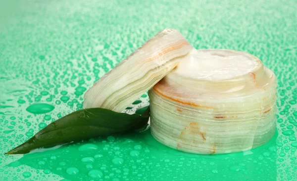 Tarro abierto de crema con hoja verde fresca sobre fondo verde con agua dr — Foto de Stock
