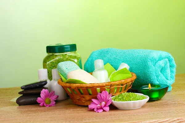Hotel amenities kit in basket on wooden table on green background — Stock Photo, Image