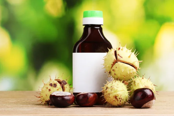 Chestnuts and medical bottle on wooden table on green background — Stock Photo, Image
