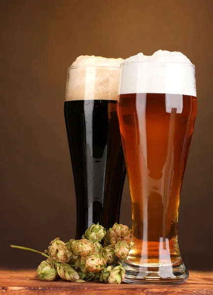Black and golden beer in glasses and hop on wooden table on brown backgroun — Stock Photo, Image