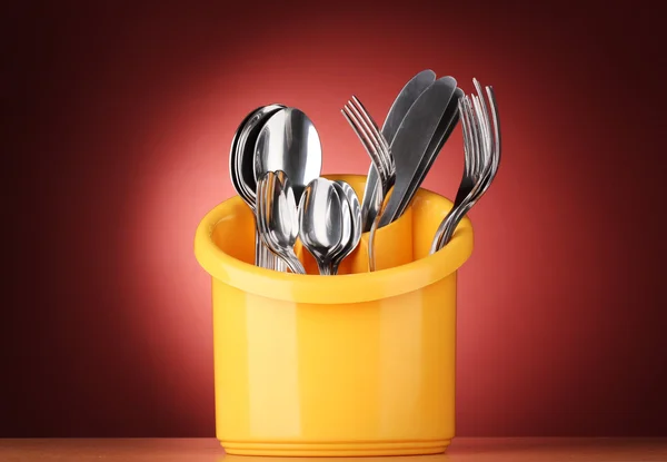 Cubertería de cocina, cuchillos, tenedores y cucharas en soporte amarillo sobre fondo rojo — Foto de Stock