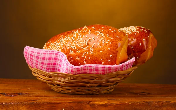 Baked bread in basket on wooden table on brown background — Stock Photo, Image