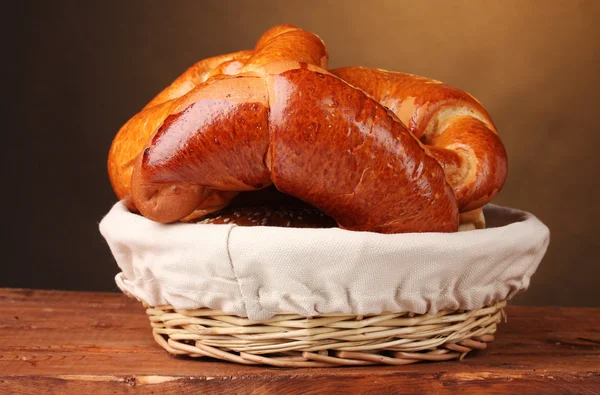 Nybakat bröd i korg på träbord på brun bakgrund — Stockfoto