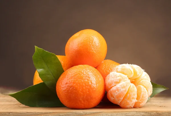 Mandarinen mit Blättern auf Holztisch auf braunem Hintergrund — Stockfoto