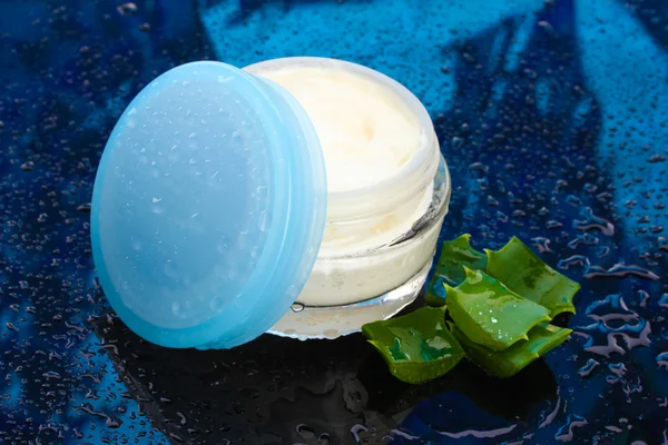 Åbnet glas krukke med fløde og aloe på mørkeblå baggrund med vanddråbe - Stock-foto