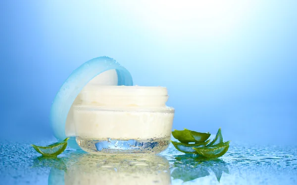Glazen pot crème of Aloë op blauwe achtergrond geopend met waterdruppeltjes — Stockfoto