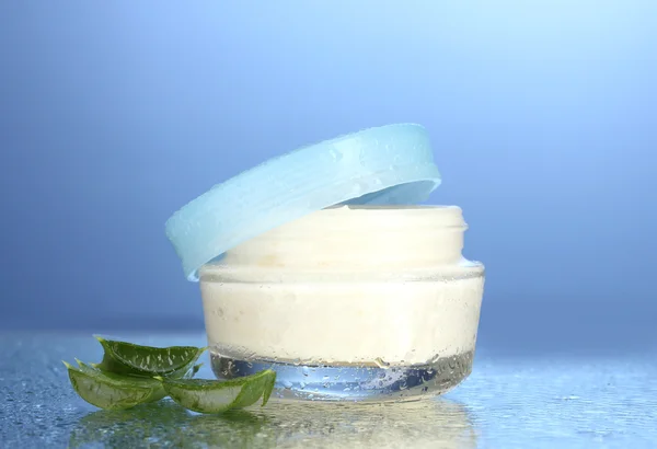 Glazen pot crème of Aloë op blauwe achtergrond geopend met waterdruppeltjes — Stockfoto