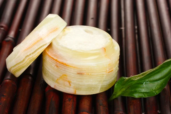 Vasetto aperto di crema con foglia verde fresca su tappetino di bambù con goccioline d'acqua — Foto Stock