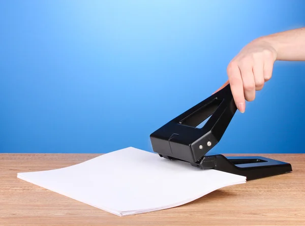 Black office hole punch with paper on blue background — Stock Photo, Image