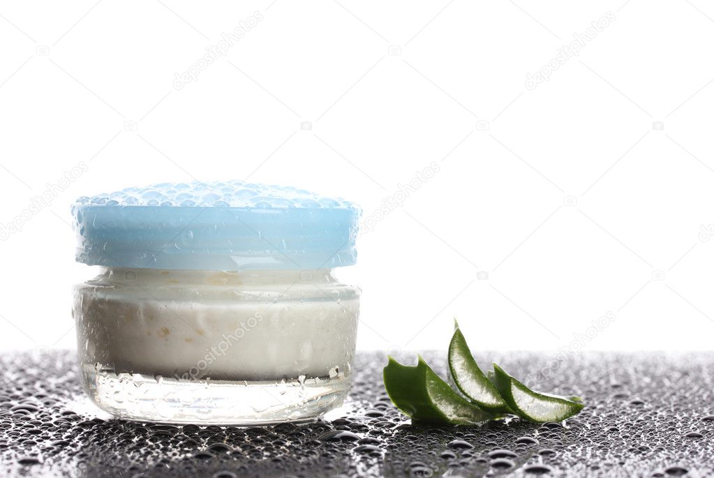 Closed glass jar of cream and aloe on black table with water droplets isola