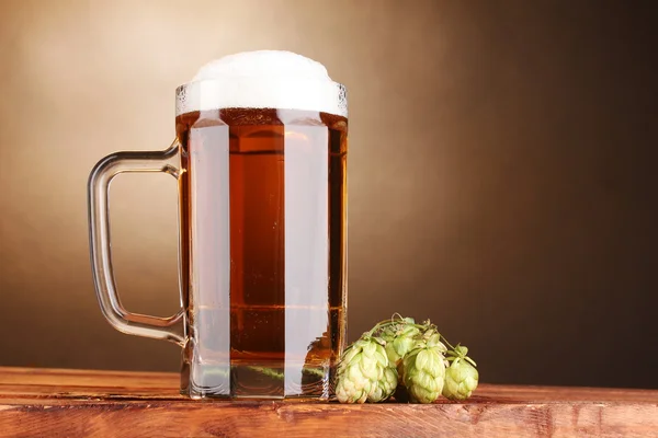 Jarra de cerveza y lúpulo verde sobre mesa de madera sobre fondo marrón —  Fotos de Stock