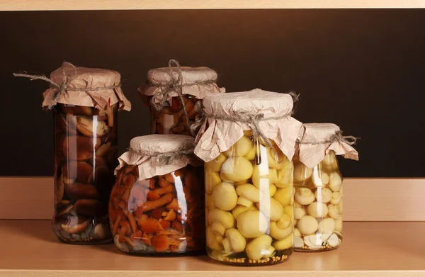 Deliciosos champiñones marinados en los frascos de vidrio en el estante de madera — Foto de Stock