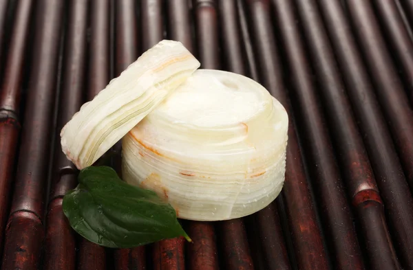 Vasetto aperto di crema con foglia verde fresca su tappetino di bambù con goccioline d'acqua — Foto Stock