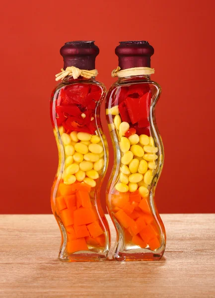 Due bottiglie con peperone rosso, fagioli, carote per arredo cucina su dorso rosso — Foto Stock