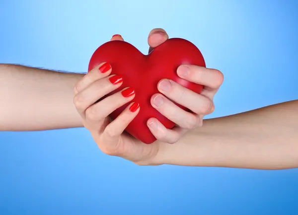 Мужчина и женщина держат в руках красное сердце на синем фоне — стоковое фото