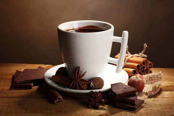 Чашка горячего шоколада, коричные палочки, орехи и шоколад на деревянном столе — стоковое фото