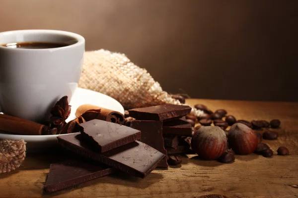 Koffie beker en bonen, kaneelstokjes, noten en chocolade op houten tafel o — Stockfoto