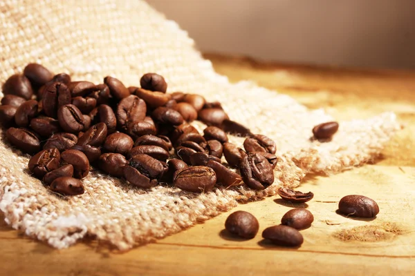 Coffee beans on sacking on wooden table — Stock Photo, Image