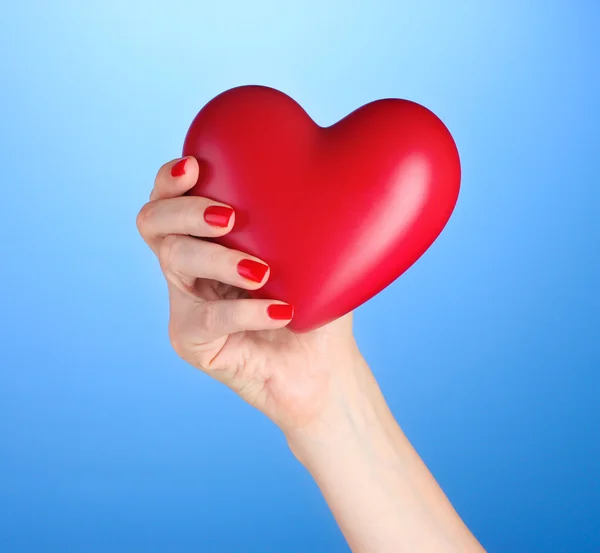 Κόκκινη καρδιά σε γυναικεία χέρια σε μπλε φόντο — Φωτογραφία Αρχείου
