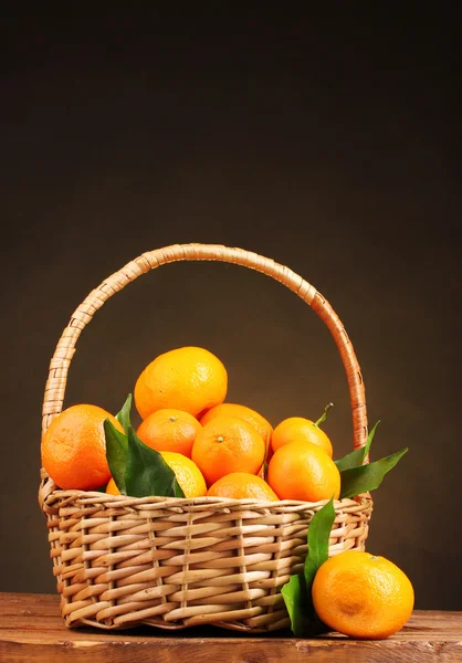 Tangerines with leaves in a beautiful basket on wooden table on brown backg Stock Image