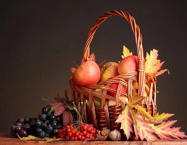 Beautiful autumn harvest in basket and leaves on brown background — Stock Photo, Image