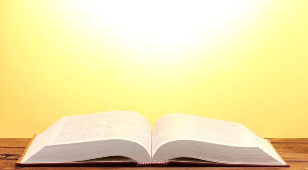 Buch aufschlagen auf Holztisch auf gelbem Hintergrund — Stockfoto