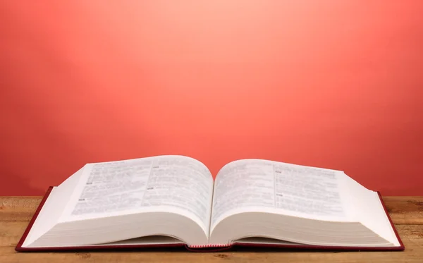 Open boek op houten tafel op rode achtergrond — Stockfoto