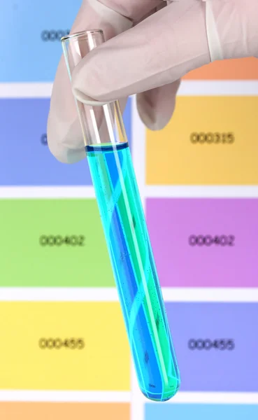 Tubo con líquido azul en la mano sobre el fondo de muestras de color — Foto de Stock