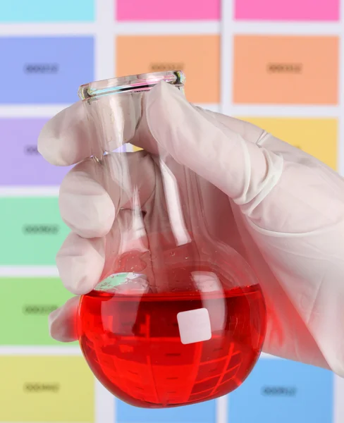 Baňka s červenou tekutinu v ruce na barvu vzorky pozadí — Stock fotografie