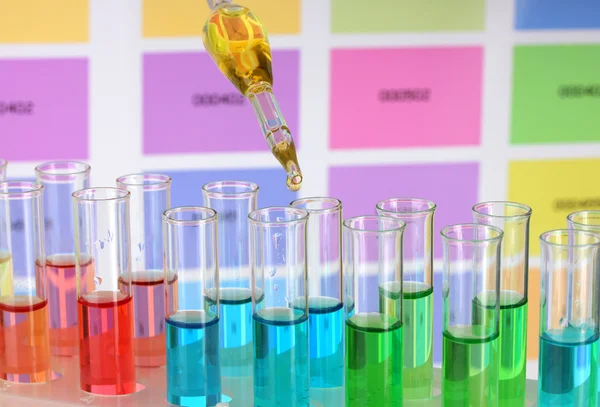 Тестовые трубки с цветной жидкостью и пипеткой на фоне цветных образцов — стоковое фото
