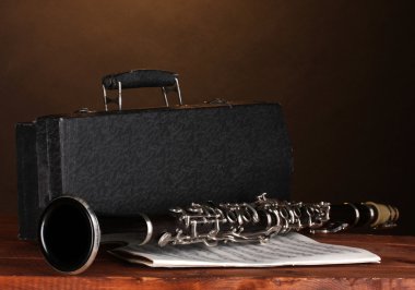 Old clarinet, case and notebook with notes on wooden table on brown backgro clipart