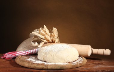 Dough and bags with flour on wooden table on brown background clipart